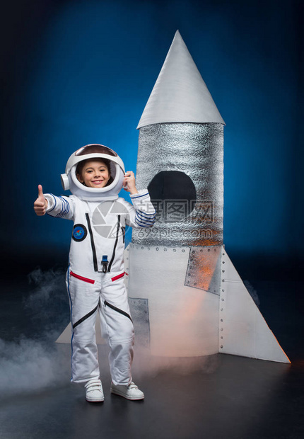 穿着宇航员服装微笑的小女孩站在发射火箭附近图片