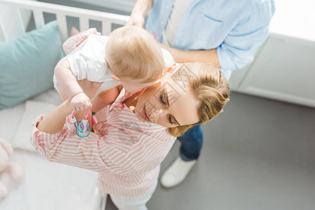 母亲从婴儿床养育幼女父亲站在附近图片