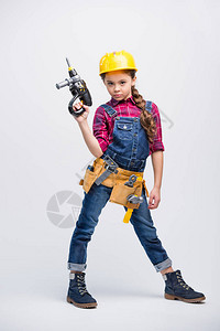 身着工具带和硬帽的小女孩拿着玩具钻孔图片