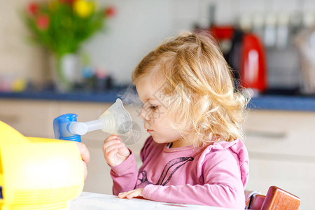 蹒跚学步的小女孩在家里用雾化器吸入帮助和拿着设备的父亲或母亲孩子有流感咳嗽和支气管炎哮喘吸入器吸背景图片