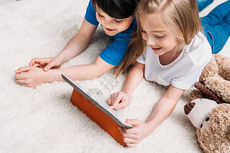 男女儿童在家里躺在地毯上玩数字平板电脑图片