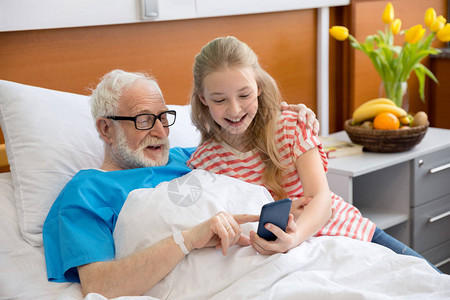 在医院床上使用智能电话的病人祖父和儿童的病图片