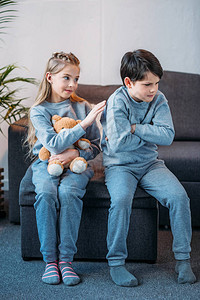 可爱的小女孩抱着泰迪熊却坐在家里沙发上背图片