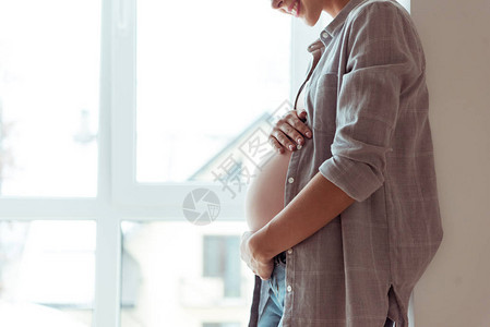 以手放在肚子上站在窗户边站着的微笑怀孕妇女图片