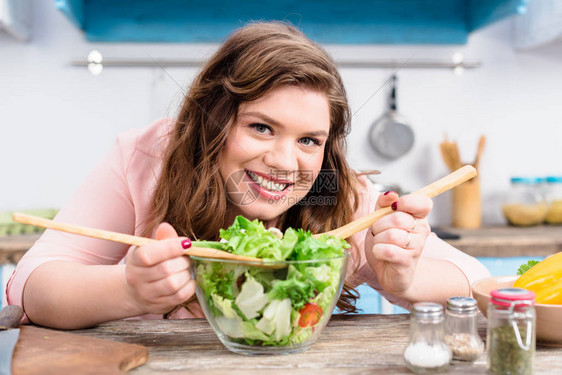 超重笑容女肖像在家中厨房煮新鲜沙拉做晚饭时图片