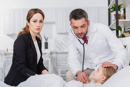 身穿白大衣的儿科医生在家中用听诊器检查生病的孩子妈图片