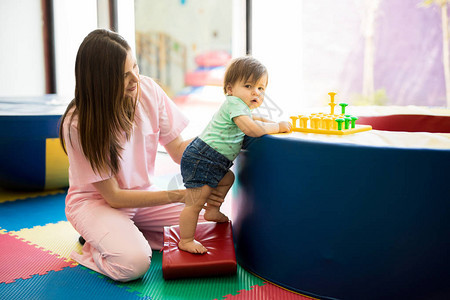 一个西班牙裔婴儿在童治疗中心玩耍时站立并练习保图片