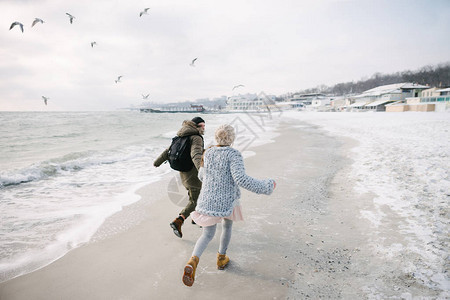 年轻夫妇牵着手在冬季海边奔跑的背影图片