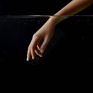 女孩将手伸入清澈的水中在黑的和黑色的背景图片