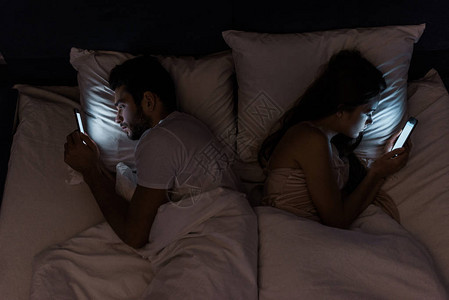 晚上躺在床上使用智能手机的年轻受挫夫图片