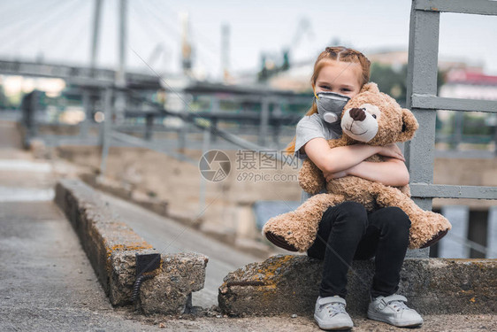 在街上抱着Teddy熊的儿童保护面罩图片