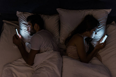 晚上躺在床上使用智能手机的年轻夫妇图片