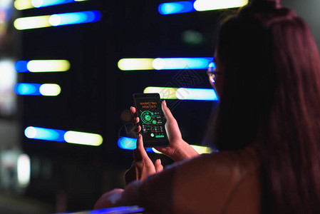晚上霓虹灯街上手持带营销分析设备的智能手机的女孩背影图片