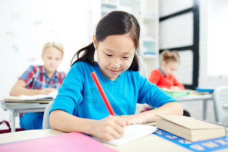 亚洲小学生在课堂上用红色蜡笔在纸上画图片