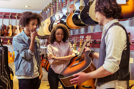 美丽的年轻非裔美国夫妇站在一家音乐店里选择一把吉他拿着吉图片