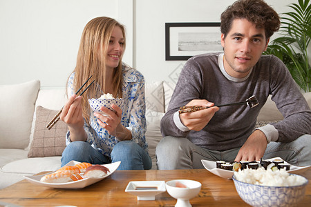 有吸引力的年轻夫妇喜欢在家吃日本寿司和maki食物图片