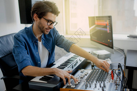 音乐制作人正在录音室的合成器键盘和电脑上创作一首歌曲人在录音室工作混音器或DJ在广图片