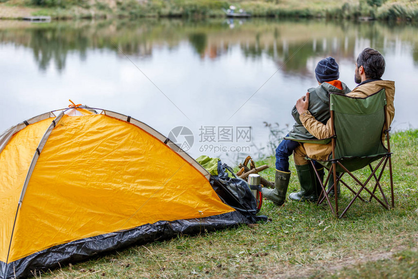 父亲和儿子坐在湖边帐篷露营的背影图片