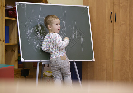 有创意的小男孩在幼儿园教室的黑板上画图片