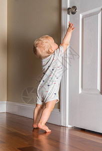 大约12个月大的幼儿婴试图接近门把手以逃离房间背景图片