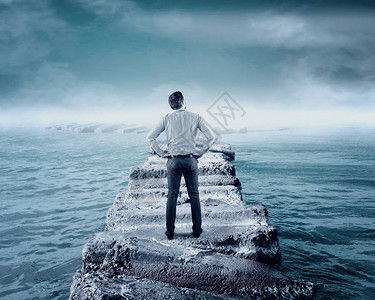商人站在海中岩石的浮船上站立图片