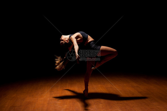 一位美丽的爵士舞女者在聚光灯下的黑暗舞台上表演时展示她的舞蹈图片