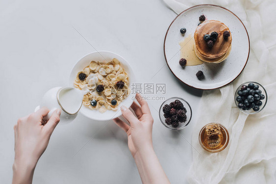 早餐时人们在碗里倒牛奶和麦片的俯视图图片