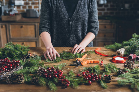 设计师在工作场所制作圣诞花环装饰浆果和松锥形松果的图片