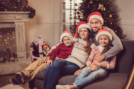 穿着圣达克休斯帽子的年轻家庭在圣诞节前夕在家里沙图片