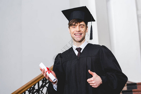 穿着毕业礼服的快乐学生微笑同时持有文图片