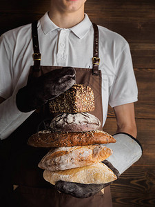 各种新鲜出炉的面包在年轻的面包师手中时髦的北欧面包师用黑麦图片
