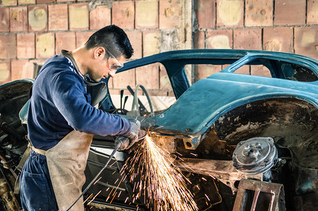 年轻机械工人在凌乱的车库里修理一辆旧的老式汽车身图片