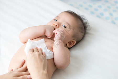 妈在更换尿布或尿布以及擦手脸或腿时用湿纸巾清洁和擦拭身体婴儿图片