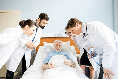 专业年轻医生在病床上使用数字平板电脑看老年患者图片