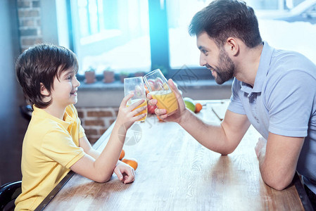 笑着的小男孩和他父亲在餐桌上用果汁图片