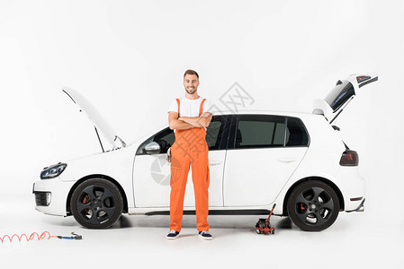 微笑英俊的汽车修理工交叉双臂站在白色的破车旁图片