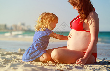 可爱的小女孩在沙滩上听妈妈的肚子图片
