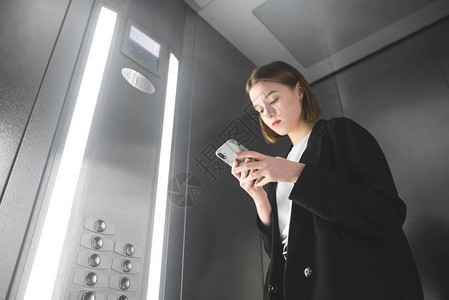 女上班族正在电梯里看着她的智能手机屏幕女商人在电梯里检查手机上的消图片