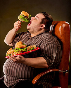 吃快餐汉堡包的胖子的饮食失败快乐的微笑超重的人通过在叉子上吃巨大的汉堡包而破坏了健康食品无限丰富的食物男人在结图片