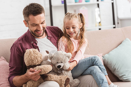 父亲和女儿在父亲膝盖上玩泰迪熊图片