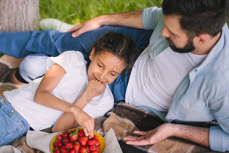 快乐的父亲和女儿吃草莓在野餐时躺图片
