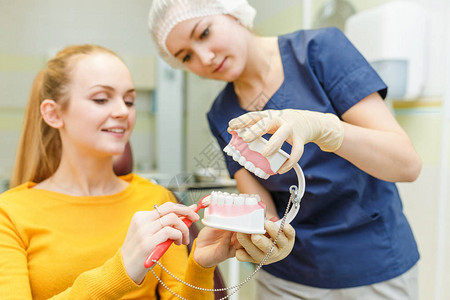 拥有下巴模型和刷子的年轻牙医向病人解释口腔和牙齿图片