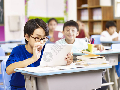亚洲小学生好奇地看着他同学拿着的平板电脑图片