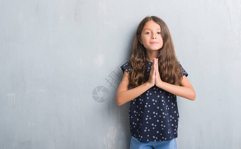 年轻的西班牙小孩在灰墙上乞讨用双手一起祈祷请求宽恕微笑着满背景图片