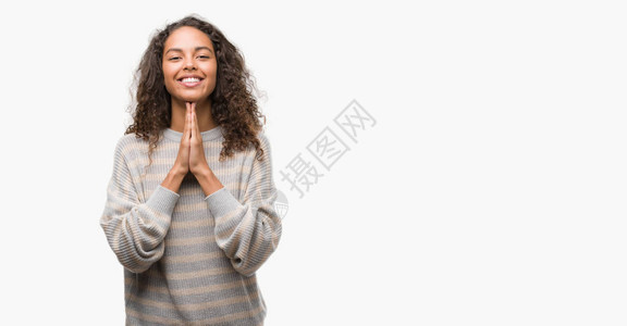 美丽的年轻西班牙女人穿着条纹毛衣用双手一起祈祷祈求宽恕微笑着满怀信图片