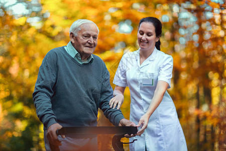 在秋季公园帮助老年男子的年轻护士老年人在户外用助老图片