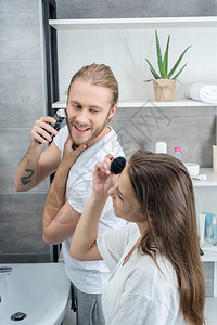 快乐的丈夫刮胡子妻子早上在洗手间施面图片