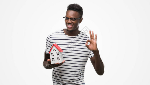 年轻非洲男子拿着房子做得很好的标志用手指图片