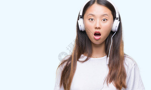 戴着耳机听音乐的亚洲年轻女与世隔绝的背景被惊吓得惊吓到图片