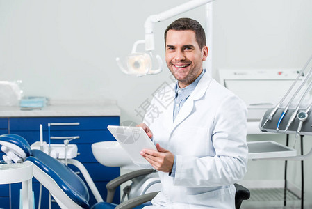 穿着白外套的快乐牙医在牙科诊所持图片